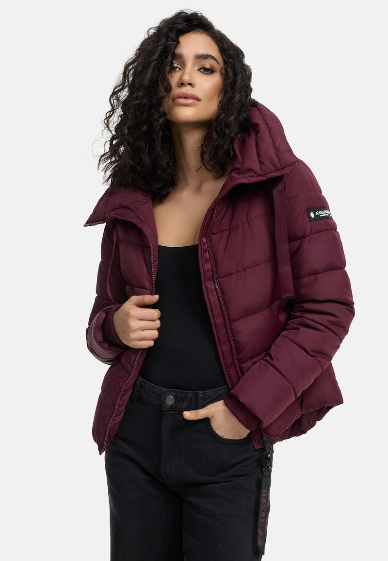 Bordeaux pufferjack met een capuchon, voorzien van een ritssluiting, een doorgestikt ontwerp en elastische manchetten. Zwarte broek maakt de outfit compleet.
