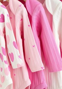 Kolme pitkähihasta paitaa eri pinkin sävyissä, mukaan lukien valkoinen paita, jossa on suuria pinkkejä sydämiä, ja kaksi tekstuurilla varustettua pinkkiä vaihtoehtoa, joissa on pieniä sydänkoristeita.