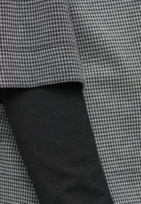 Czarna i biała tkanina w wzór houndstooth o teksturowanej powierzchni, połączona z gładkim, jednolitym czarnym rękawem.