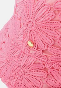 Rosa virkad väska med blommönster, texturerad yta och en detalj i guld. Den mjuka tygbotten kompletterar den intrikata designen.