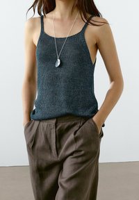 Dark blue knitted tank top with spaghetti straps, paired with light brown loose-fit pants. Features a simple, minimalistic design.