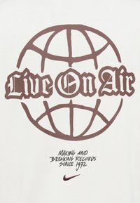 Λευκό βαμβακερό t-shirt με μεγάλο καφέ γραφικό της υδρογείου και έντονο κείμενο "Live On Air". Περιλαμβάνει το κείμενο "Making and Breaking Records Since 1972" από κάτω.