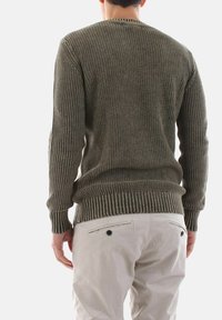 Maglione a coste di colore verde oliva con colletto tondo, caratterizzato da maniche lunghe e orlo aderente. Indossato con pantaloni chiari.