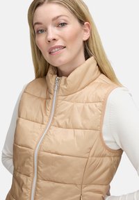 Lichte gewatteerde vest in zacht beige, met een hoge kraag, frontzipper en horizontaal gestikt ontwerp voor warmte en comfort.