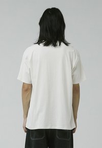 Tricou alb cu mânecă scurtă, realizat din bumbac, cu gât rotund și o croială lejeră. Fără logo-uri sau modele vizibile.