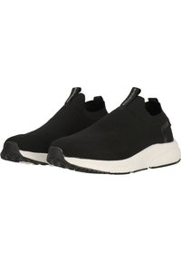 Mustat slip-on-tennarit, joissa on tekstuurinen neulepinta, valkoinen välipohja ja musta kumipohja. Takana on vetotapit, jotka helpottavat pukemista.