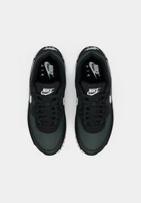 Svarta Nike-sneakers i mesh och läder, med en texturerad ovandel, svarta snörningar och vita logotypaccenter på sidorna och tungan.