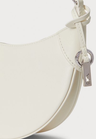 Mala de couro creme com forma curva, costura bordada nas bordas e uma etiqueta de ferragem prateada com um pequeno detalhe de logo.