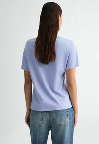 T-shirt lilas à manches courtes avec un col rond, texture lisse et coupe décontractée, porté avec un jean taille haute bleu clair.