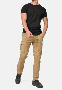 Czarny bawełniany t-shirt z krótkim rękawem zestawiony z beżowymi spodniami typu cargo z bocznymi kieszeniami, noszony z czarnymi trampkami. Gładki materiał i swobodny krój.