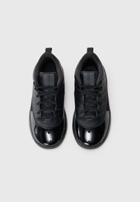 Et par svarte lave sneakers med glanset tåhette og snøringer på en helt hvit bakgrunn.