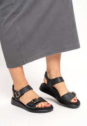 Black leather sandals with two adjustable straps, a textured finish, and a thick black sole. Features metal buckle accents and open heel design.