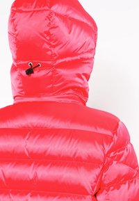 Veste rembourrée rouge vif avec capuche, présentant une texture de tissu lisse et brillante ainsi que des coutures horizontales visibles. Système de réglage sur la capuche.