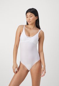 Hvit bodysuit med dyp utringning, tynne stropper og gjennomsiktig stoff. Designet for en tettsittende silhuett med et minimalistisk utseende.