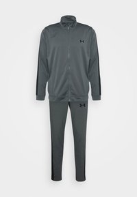 Survêtement Under Armour gris foncé avec veste zippée intégrale, bandes noires sur les côtés et logo sur la poitrine et la cuisse du pantalon.