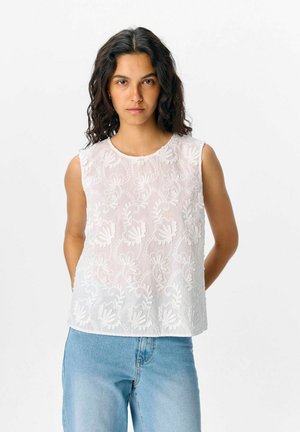 White sleeveless top with embroidered floral design. Lightweight, sheer fabric; round neckline; slightly loose fit; paired with light blue jeans.