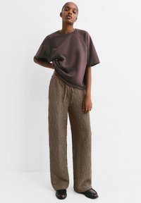 Top marrone scuro, a maniche corte e dalla vestibilità morbida, con scollatura rotonda, abbinato a pantaloni larghi di tessuto marrone chiaro. Scarpe nere basse.