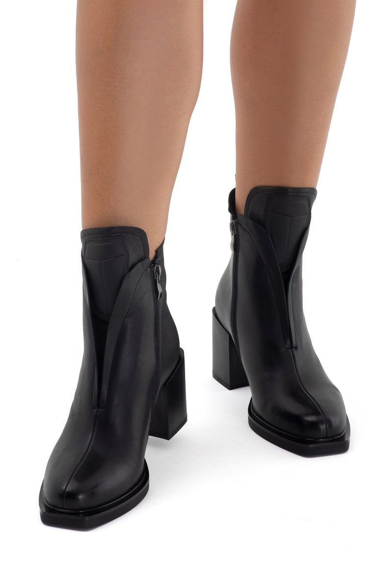 Stivali alla caviglia neri in pelle liscia, con una zip diagonale, punta quadrata e tacco a blocco per maggiore stabilità.