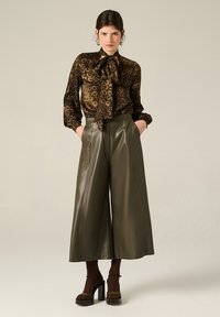 Blusa marrone a fantasia con dettaglio neck-tie, abbinata a pantaloni a gamba larga in faux pelle verde oliva a vita alta e tacchi a plateau.