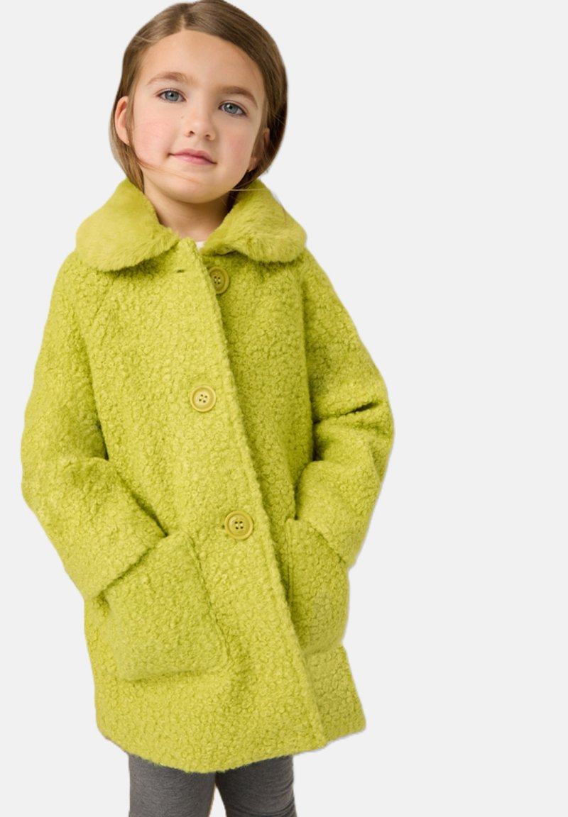 Cappotto verde lime brillante con texture, caratterizzato da un morbido colletto in pelliccia, ampie tasche frontali e chiusure con bottoni, indossato sopra leggings grigi.
