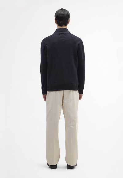 Navy knit pullover with a collar, back seam detail, paired with cream wide-leg trousers and black shoes. Clean, minimalist design.
