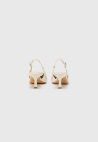 Kremfargede slingback-hæler med en avsmalnet blokkhæl, med en glatt lakkfinish og justerbar ankelrem.