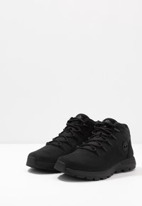 Chaussures de randonnée noires avec une texture lisse, un col rembourré et une semelle coussinée. Présente un design à lacets et un logo sur le talon.