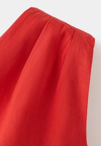 Gros plan d'un tissu rouge vif avec une couture froncée, montrant la texture et des plis doux sur un fond clair uni.