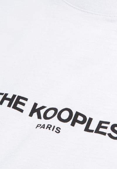 Balts kokvilnas T-krekls ar melnu tekstu, kas lasāms "THE KOOPLES" un "PARIS", ar klasisku laukuma kakla izgriezumu un gludu tekst�ūru.