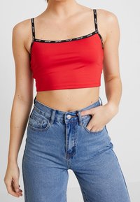 Top court rouge avec logo Levi's noir sur les bretelles, associé à un jean bleu taille haute avec poches avant et fermeture par bouton.