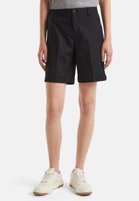 Černé bavlněné šortky s klasickým designem, s přehnutým lemem, poutky na opasek a bočními kapsami, v kombinaci s bílými teniskami.