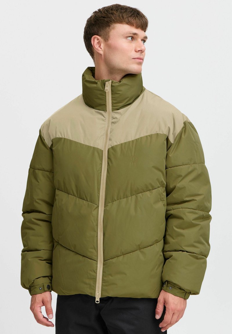 Chaqueta acolchada verde y beige con un alto cuello, cierre de cremallera frontal y un diseño de panel geométrico en contraste. Tejido suave con textura acolchada.