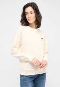 Felpa color crema con colletto rotondo e maniche lunghe. Presenta un piccolo design ricamato sul petto. Materiale in cotone.