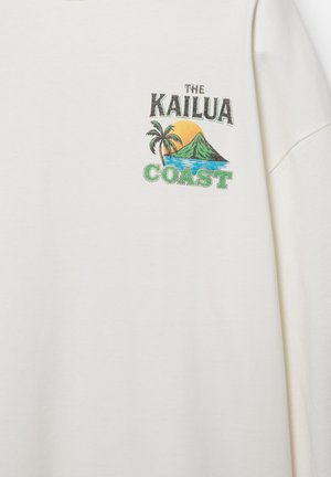 Fehér ing színes grafikával, amelyen pálmafát, hegyet, naplementét, óceánt és a „The Kailua Coast” szöveget látni a mellkasnál.