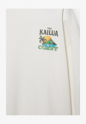 Fehér ing színes grafikával, amelyen pálmafát, hegyet, naplementét, óceánt és a „The Kailua Coast” szöveget látni a mellkasnál.