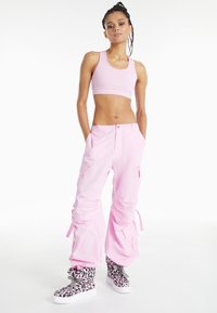 Vaaleanpunaiset cargo-housut, joissa on kireät lahkeet ja sivutaskut, yhdistettynä vastaavaan vaaleanpunaiseen crop-toppiin sekä musta-valkoisiin leopardikuvioisiin korkeisiin tennareihin.