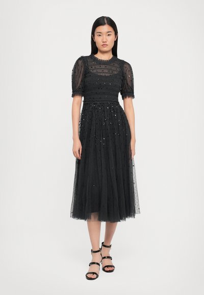Zwarte tule jurk met een getailleerde bodice, korte puffmouwen en een vloeiende rok. Versierd met kleine pailletten over de hele jurk. Zwarte sandaaltjes met straps.