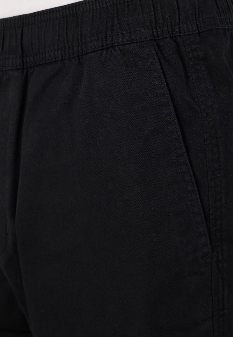 Schwarze Shorts mit elastischem Bund aus weichem Baumwollstoff, featuring Seitentaschen und leichter Textur mit gestickten Details.
