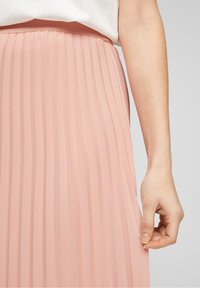 Gonna midi plissettata in morbido tessuto rosa pallido con una vita liscia. La texture è leggera e presenta linee verticali per un interesse visivo.