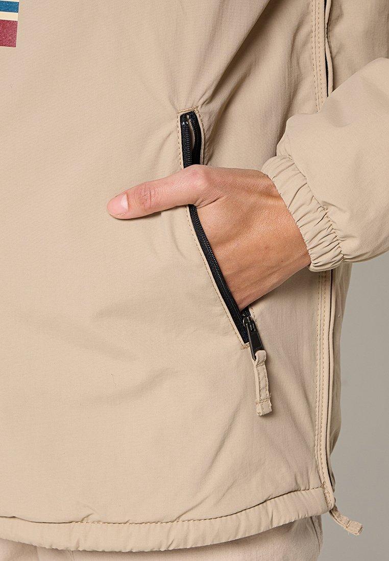 Beige lichte jas met elastische manchetten, een ritszak en een gladde textuur. Beschikt over horizontale kleurstrepen op de borst.