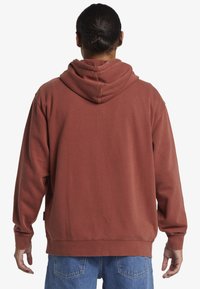 Bordová mikina s kapucňou na sťahovanie, dlhými rukávmi a voľným strihom. Mäkká tkanina s textúrovaným povrchom. Viditeľné švy na švoch.