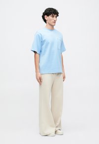 T-shirt oversized azul claro com um bolso, combinado com calças largas em tom creme e ténis brancos; tecido suave e ajuste descontraído.
