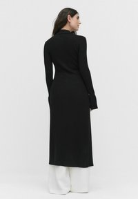 Robe en tricot côtelé noire à manches longues, silhouette ajustée et longueur longue. Dotée d'un col et de détails de poignets allongés.