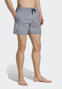 Plave plavky s bielymi pruhmi, vyrobené z ľahkej tkaniny, s elastickým pásom a šnúrkou, a postrannými vreckami.