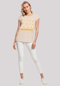 Beige t-shirt with a floral pattern in yellow and white, featuring the word "Summer" in bold, upright text. Paired with white skinny jeans.