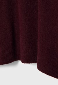 Tissu en tricot bourgogne montrant une texture avec une surface douce et duveteuse. Les bords sont finis par une coupe nette, créant une apparence lisse.