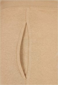 Béžové bavlněné kalhoty s boční kapsou a elastickým pasem s žebrovanými detaily, které mají hladkou texturu a jednoduchý design.
