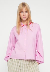 Roosa kraega särk, mille ees on nööbid ja krael tekstuuriga punane ääris. Pikkade varrukatega, elastsete mansettidega ning lõdva lõikega.