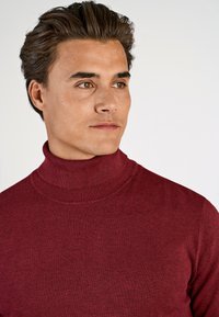 Burgundy polotröja med en ribbad krage, mjuk textur och en figursydd design som formar sig efter nacke och axlar.
