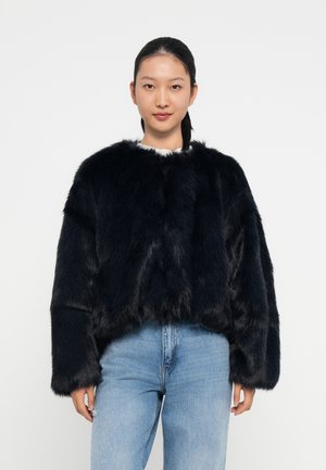 Sort faux fur cropped jakke med lange ærmer, der har en rund halsudskæring og en blød tekstur. Kombineret med blå denim jeans.